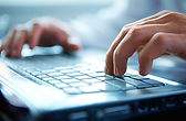Two hands type on a silver keyboard.