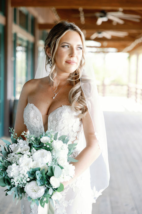 Woman in lace white gown holding a white flower bouquet looking softly to the left