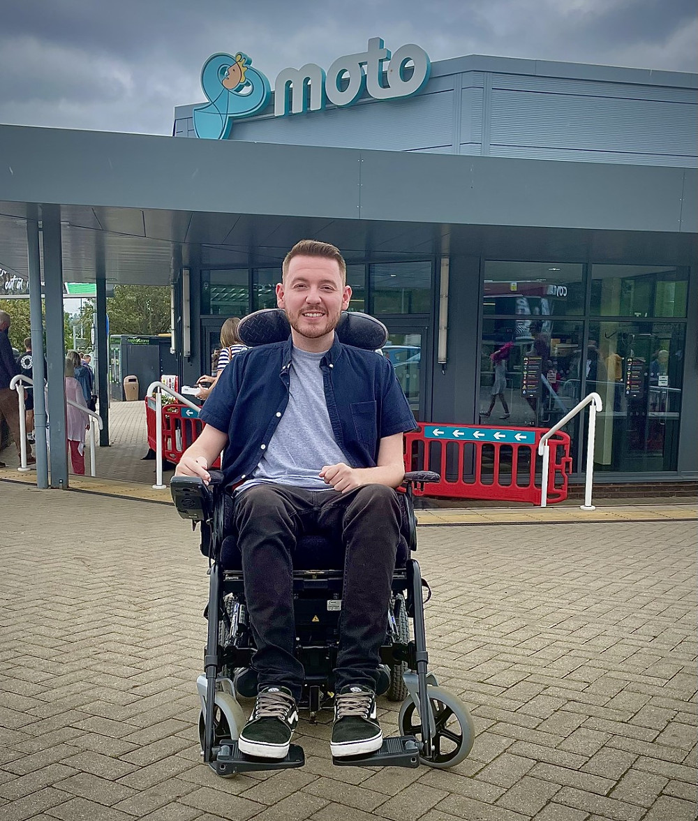Ross sat in his wheelchair, outside the main entrance sign for Exeter service station
