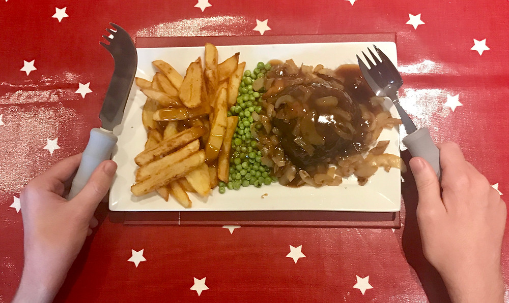 A shot of Ross's dinner (hamburger steak, chips and peas) holding a lightweight knife and fork