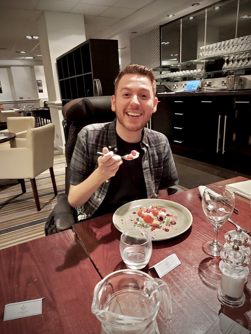 Ross sat in a restaurant smiling as he holds his spoon full of eton mess