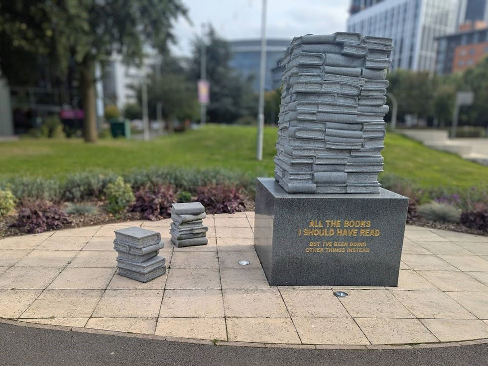 A stone sculpture featuring a pile of books with the phrase 'All the books I should have read, but I've been doing other things instead'