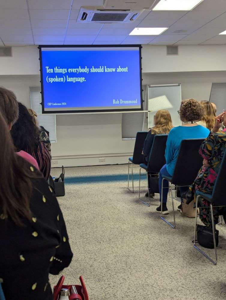 A projector screen with a blue slide and white writing 'Ten things everybody should know about (spoken) language'
