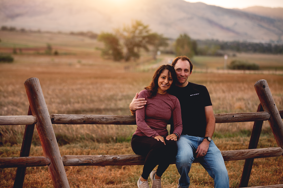 Couple sitting on a wooden fence in a rural landscape.