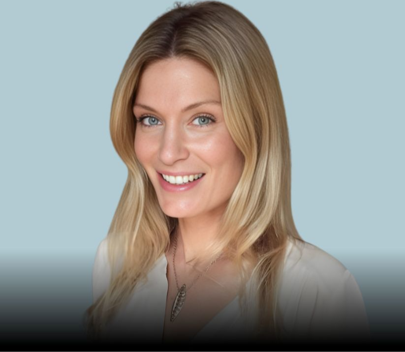 Smiling blonde woman in a white top against a pale blue background, wearing a necklace, in a bright studio portrait