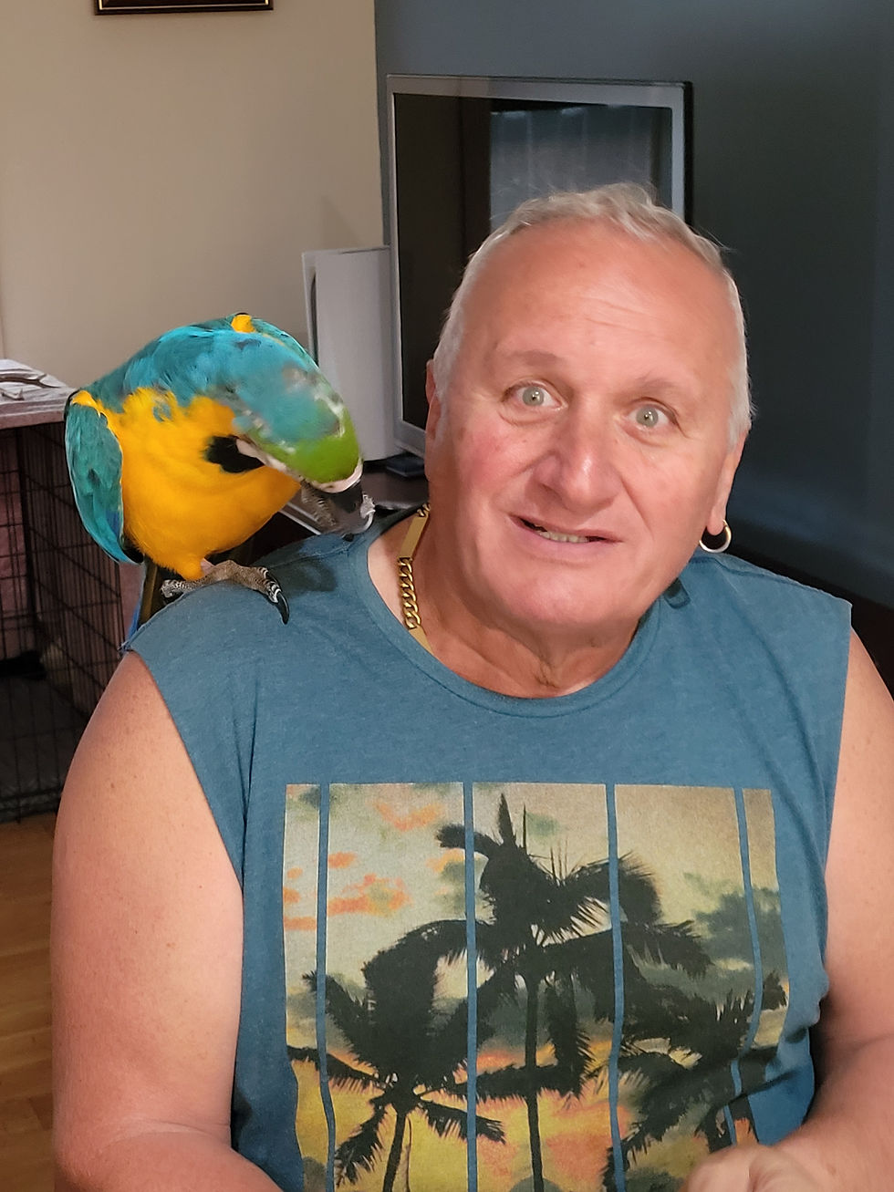 sitting down has a blue and gold Macaw on his shoulder