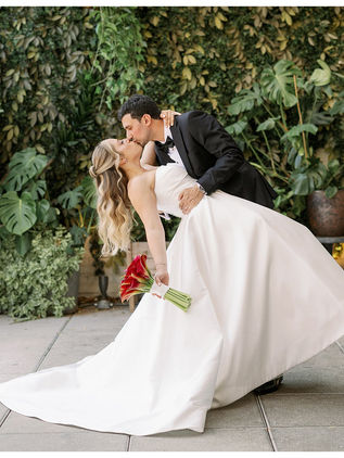 bride and groom dipping and kissing in front of live wall