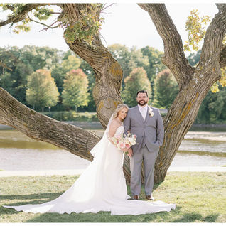 bride and groom posing under oak tree in front of a river