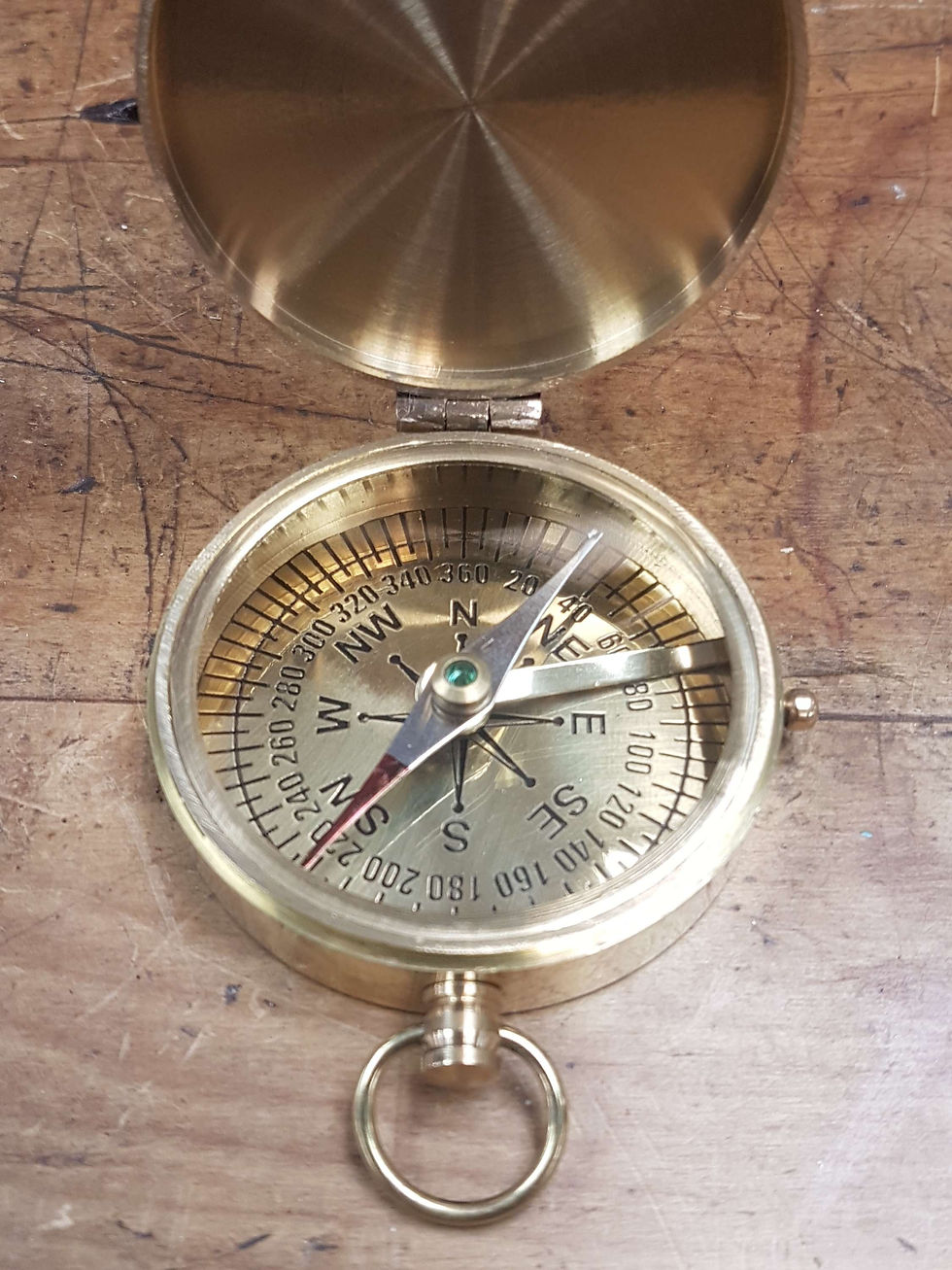 Thumbnail: Close-up of a brass compass with visible directional markings on wooden surface.