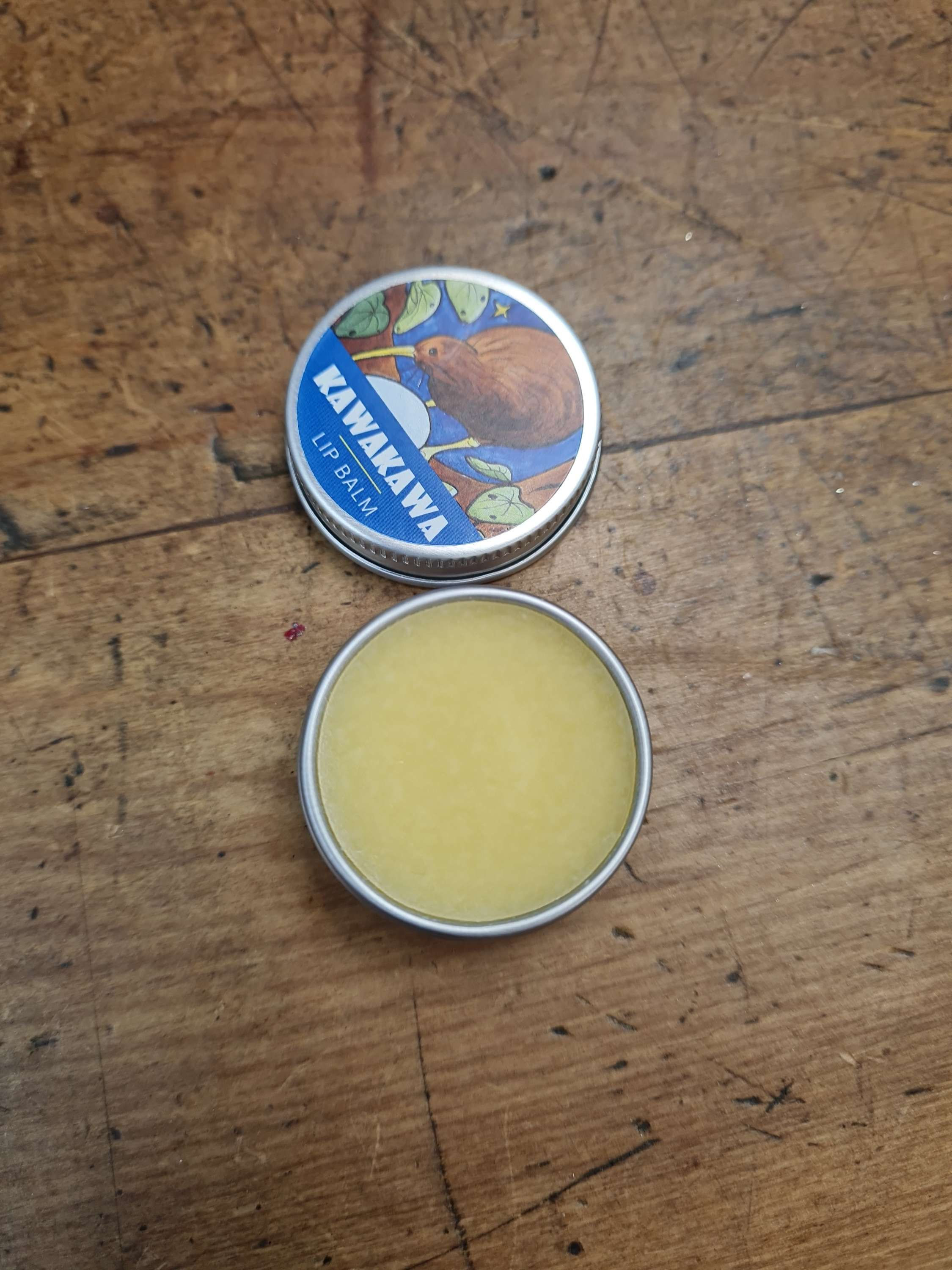 Kawakawa lip balm tin open on a wood surface, moisturizing lip balm inside.