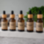 Five essential oil bottles, each labeled 'Rejuvenating Serum', with wooden tops.