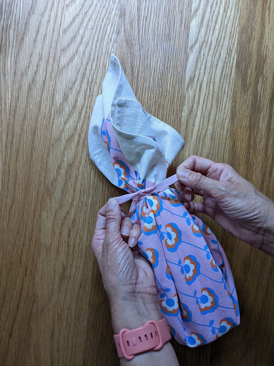 Ribbon being tied around neck of glass bottle and fabric to hold in place