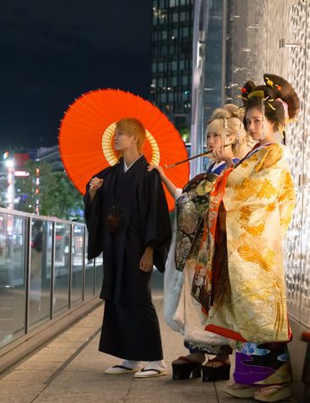 夜の街で赤い和傘を差し、華やかな着物を纏う花魁一行