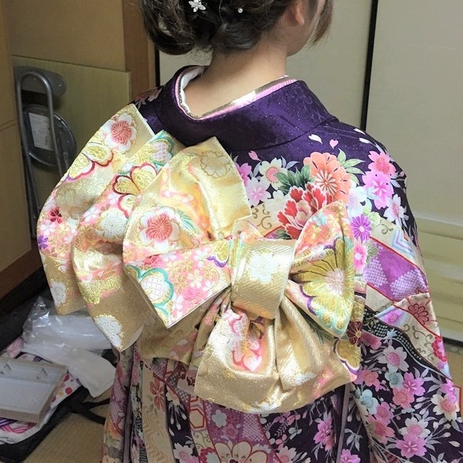 豪華な金色の帯結びと紫色の振袖の出張着付け後の後ろ姿