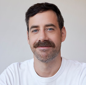 A headshot of Jean-Pierre Cloutier, a Caucasian man in his 40s with short dark hair, blue eyes, and a mustache. He is wearing a plain white T-shirt. His expression is kind and friendly.