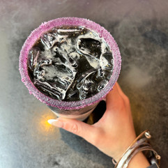 Top-down view of a charcoal iced coffee with cream swirling through it and a pink sugar rim, held in hand over a café counter at The 27 Club in Cleveland, Ohio.