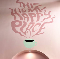 Pink wall mural reading “This is my happy place” with stylized steam rising from a pure white coffee cup, inside The 27 Club coffee shop in Cleveland, Ohio.