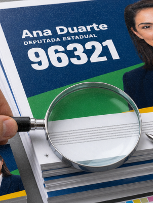 Fotografia editorial em estilo documental de uma pilha de materiais impressos de campanha (santinhos, panfletos, adesivos) sobre uma mesa de gráfica, com uma lupa ou caneta apontando para um pequeno texto legal impresso na borda de uma peça.