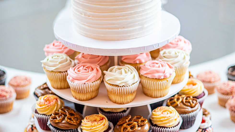 Wedding cake and cupcakes on a white tiered stand. Topper reads "Mr & Mrs Johnson." Decor and icing in pink, white, and chocolate.