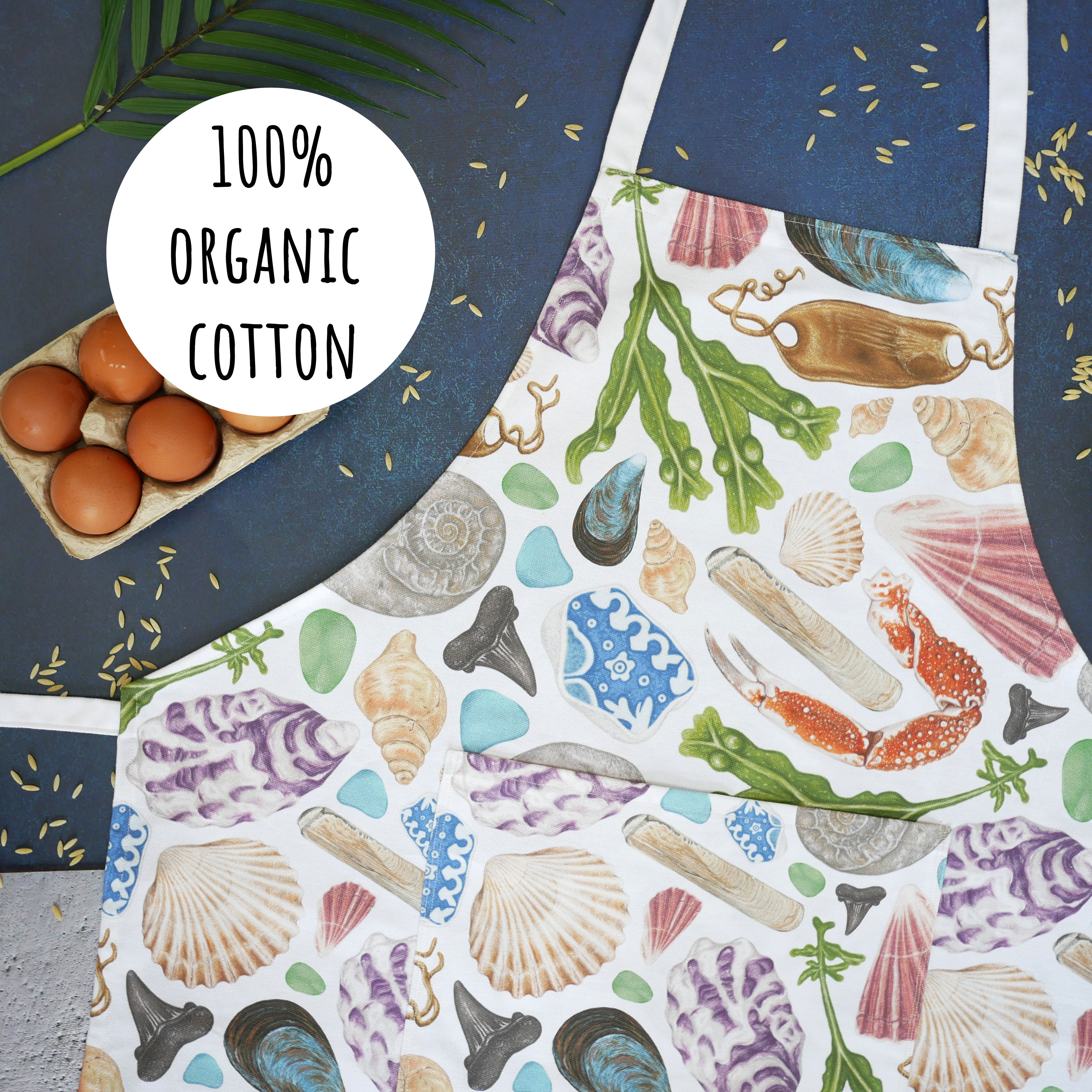 An organic cotton apron featuring illustrations of beach finds from british beachcombing