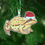 Thumbnail: A wooden Christmas tree decoration of an illustrated common frog in a santa hat. Hung on a Christmas tree