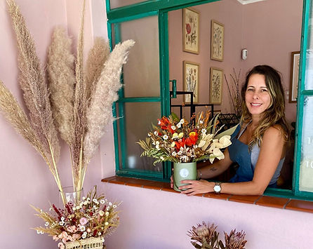 Imagem da criadora e idealizadora do pote ateliê botânico. Com um sorriso no rosto e muitas flores ao redor