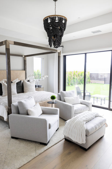 Sleek and sophisticated Los Angeles Primary Bedroom featuring a modern black canopy bed frame, accent chairs and boho chandelier.