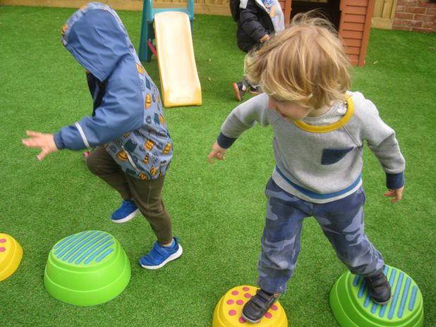 Children practise balancing and stepping across outdoor equipment to develop gross motor skills and confidence.