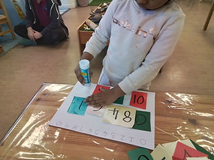 Child gluing coloured number cards onto a worksheet to support early numeracy and number recognition.