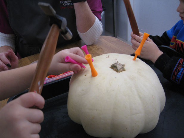 Children use tools to tap pegs into a pumpkin, strengthening hand muscles and hand–eye coordination.