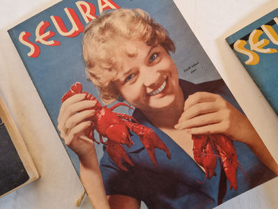 Vanha Seura-lehden kansi vuodelta 1957 esittää hymyilevän naisen sinisessä mekossa pitelemässä kahta punaista rapua.
