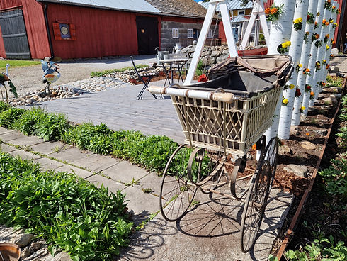 Kierrätysmateriaaleista suunniteltu vanha pihapiiri, kiviaita, puro, vanhat rottinkivaunut, pihakeinu, puutarhakalusto