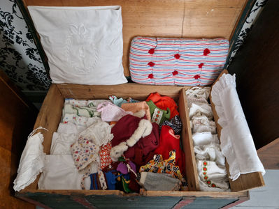 Antiikkinuken vaatteita ja kenkiä vanhassa kapioarkussa jonka väri on vihreä ja siinä on kukkakoristemaalaus