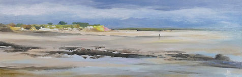 Paysage de plage à marée basse sous ciel nuageux, roches sombres au premier plan et silhouette lointaine sur sable humide.