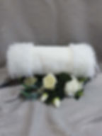 A white, faux fur muff for a winter wedding. The muff sits on a wreath of white roses.