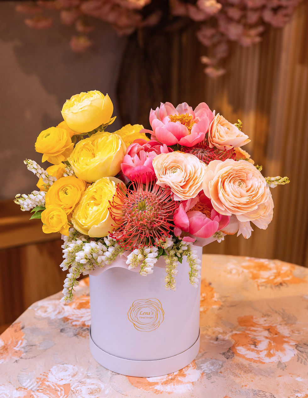 Thumbnail: Yellow and peach roses, ranunculus and peonies with accented greenry in a white hatbox handmade by Lena in Toronto