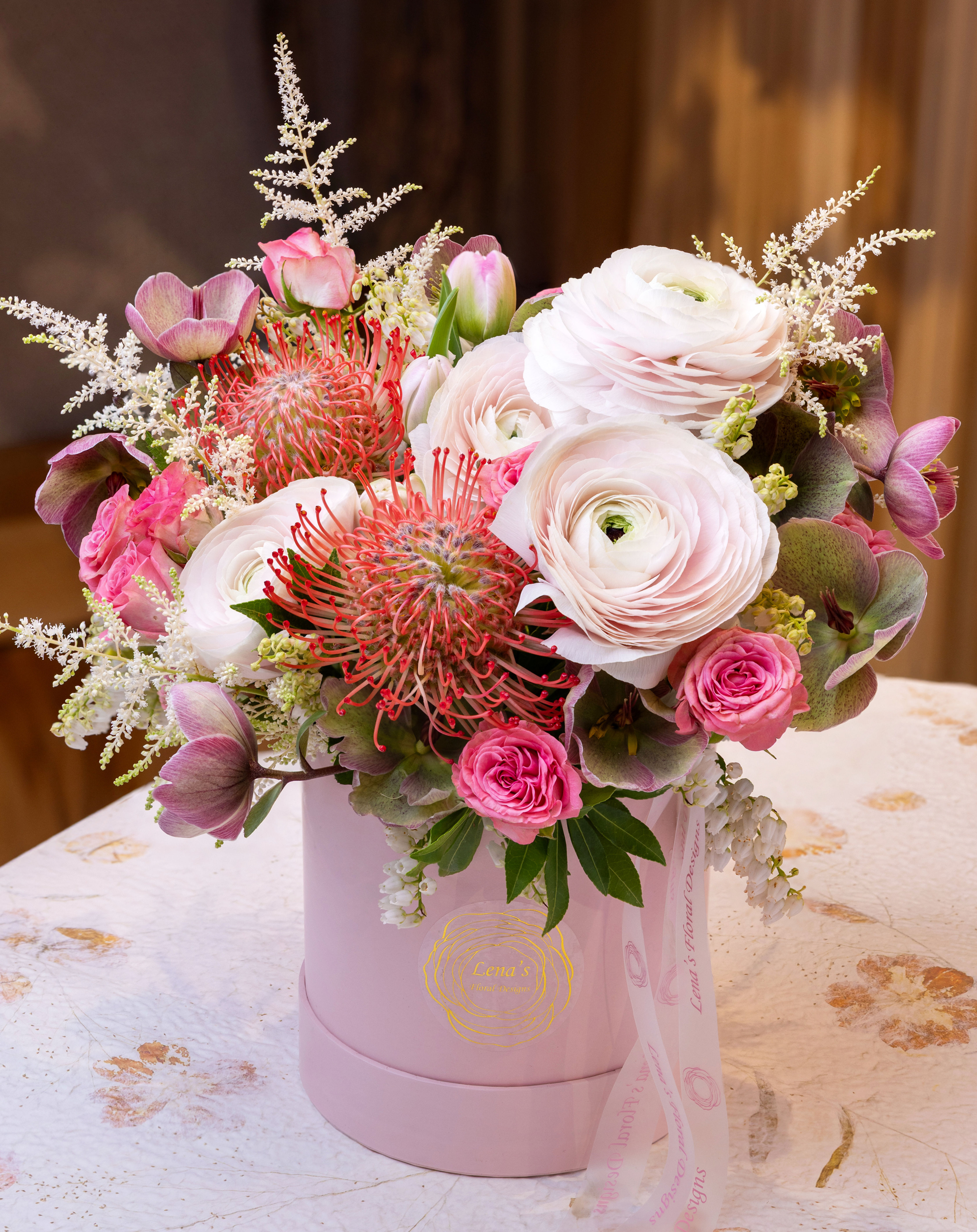 Zoom in of pink ranunculus, spray roses and helleborus with accented greenery in a pink hatbox handmade by Lena in Toronto.