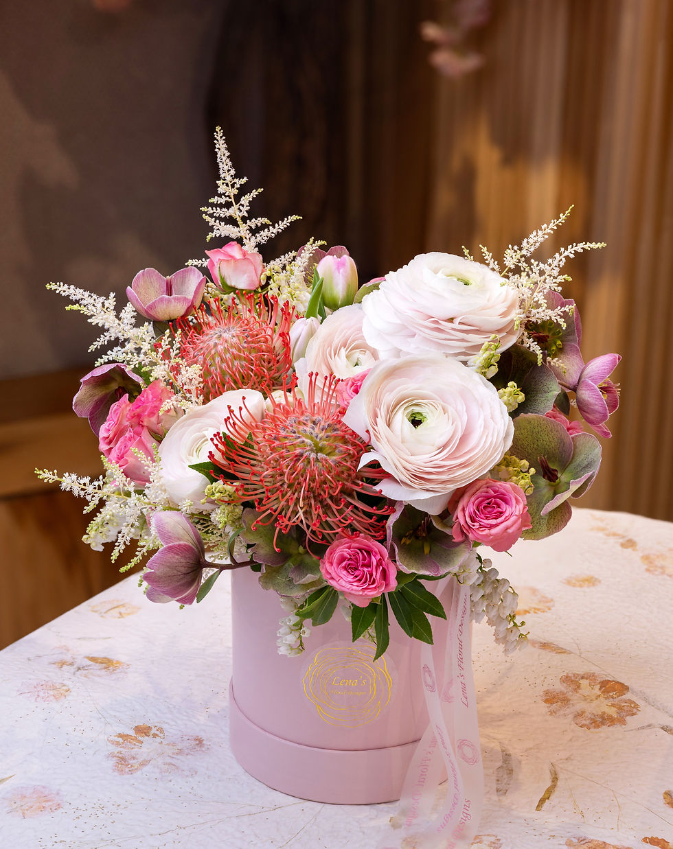 Thumbnail: Pink ranunculus, spray roses and helleborus with accented greenery in a pink hatbox handmade by Lena in Toronto.