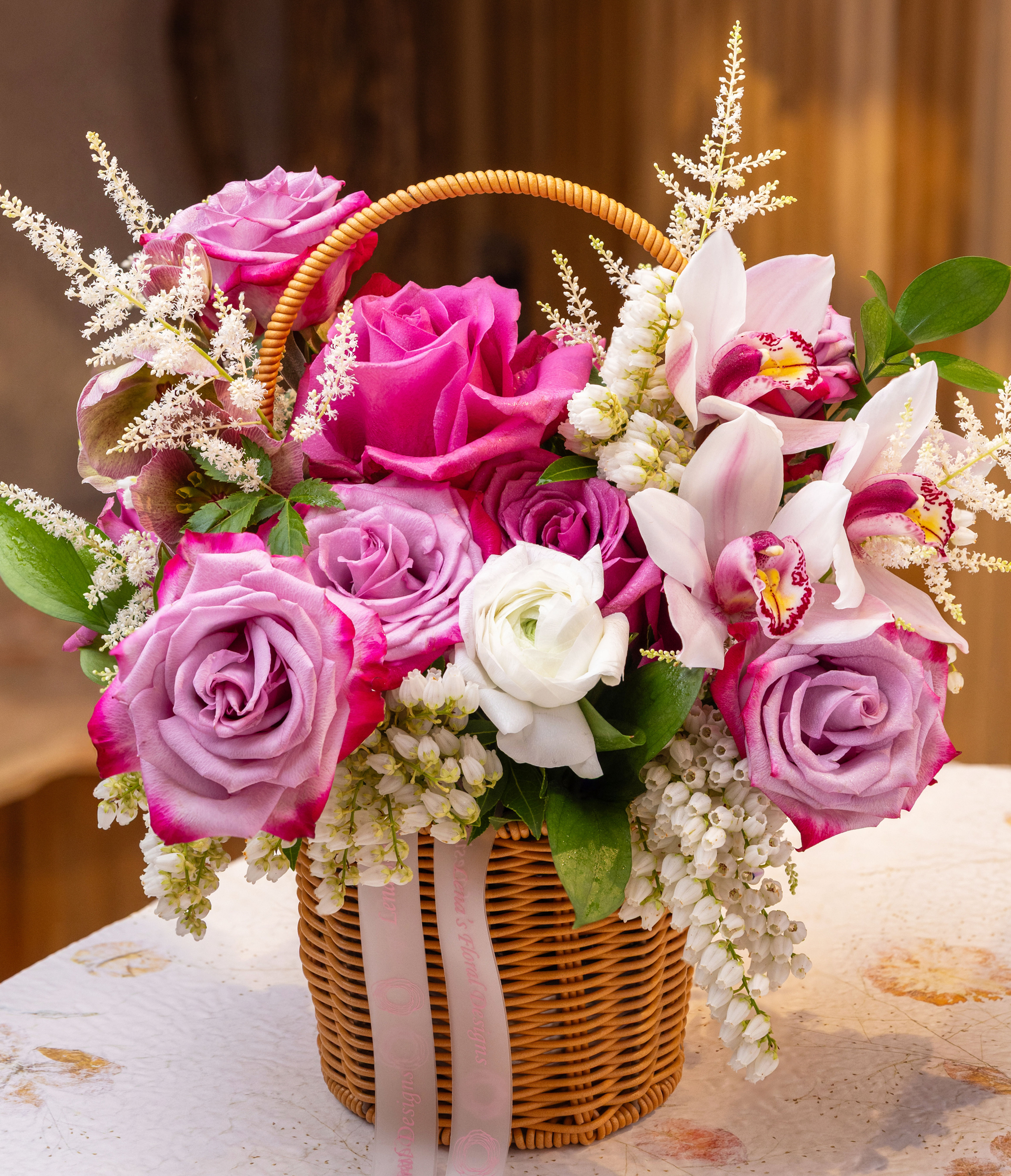 Zoom in  of pink and white roses, ranunculus and orchids with accented greens in a woven basket handmade by Lena in Toronto