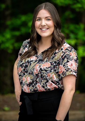 Smiling woman wearing floral blouse against a blurred green background.