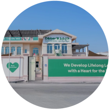 A school building with "Dibber" sign, green and white facade, and text "We Develop Lifelong Learners with a Heart for the World" on wall.