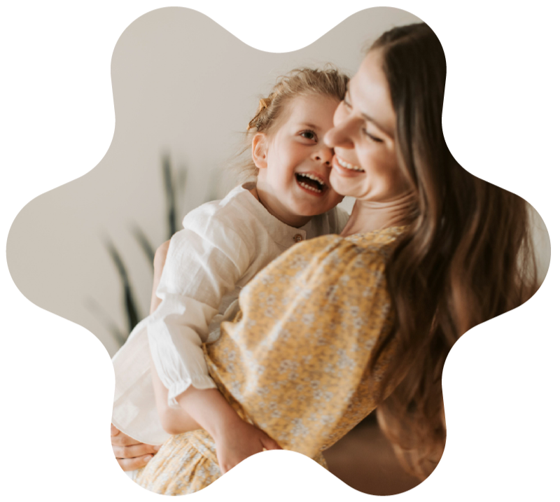 Woman in a yellow dress joyfully holds a smiling child. Soft background with green plant, conveying warmth and happiness.