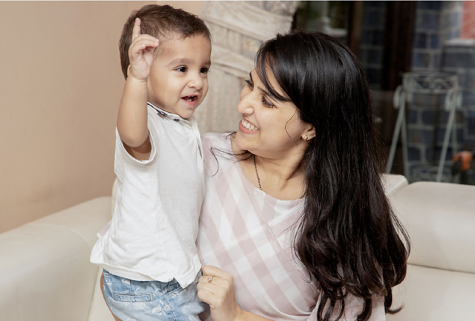 Smiling woman holding a young child who is pointing upward on a white couch. Warm indoor setting, joyful mood.
