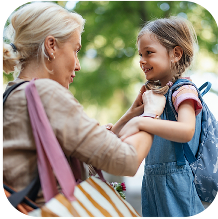 Woman kneeling, adjusting backpack straps for smiling girl outdoors. Green, blurred background; both appear happy and engaged.