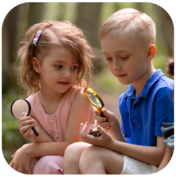Young girl and boy outdoors studying a tiny object with magnifying glasses, looking curious and focused.