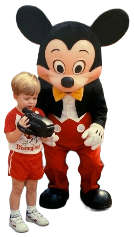 Young Michael holding a camcorder beside Mickey Mouse