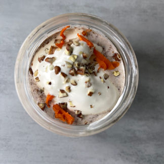 A jar of carrot cake overnight oats topped with chopped pecans and whipped cream, with visible grated carrots and a creamy, spiced oat texture.