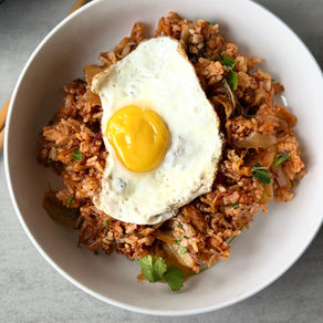 Skillet of kimchi ginger fried rice with visible pieces of kimchi, red onion, and ginger, lightly crisped, topped with a fried egg and served warm in natural light.