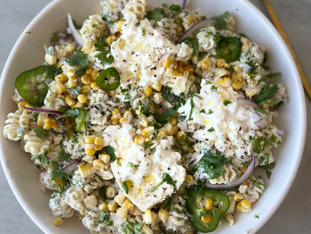 A bowl of creamy Mexican street corn pasta salad with corn, herbs, jalapenos, and burrata, styled as a summer BBQ side dish.