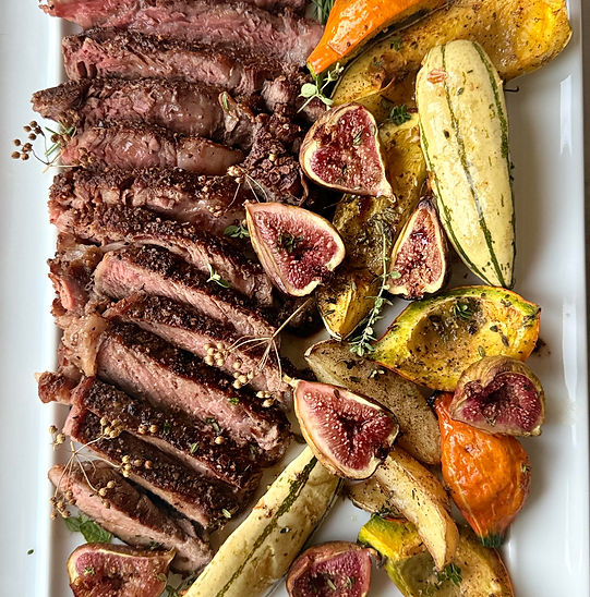Overhead view of a plated ribeye steak surrounded by golden roasted kuri and delicata squash, Yukon potatoes, and halved figs. Garnished with fresh thyme and rosemary on a rustic ceramic plate with soft natural lighting.
